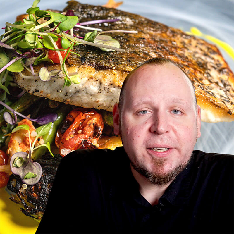 Chef John Creger standing behind a large platter of grilled fish and vegetables